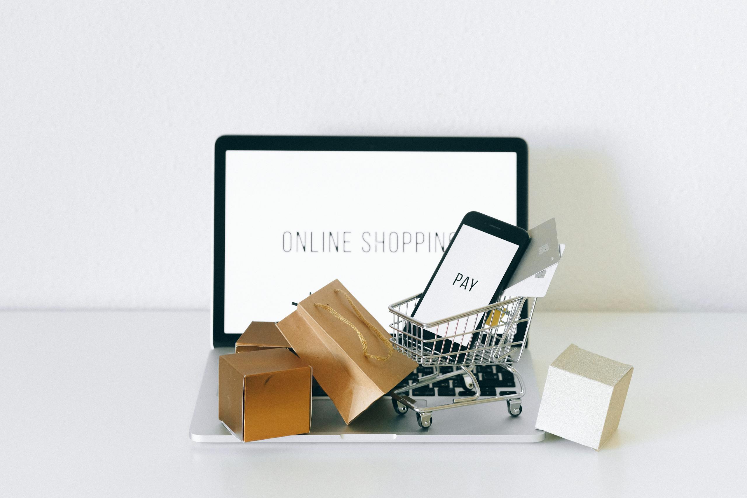 Représentation de l’achat en ligne avec un ordinateur sur lequel se trouve un panier miniature et des outils de paiements.