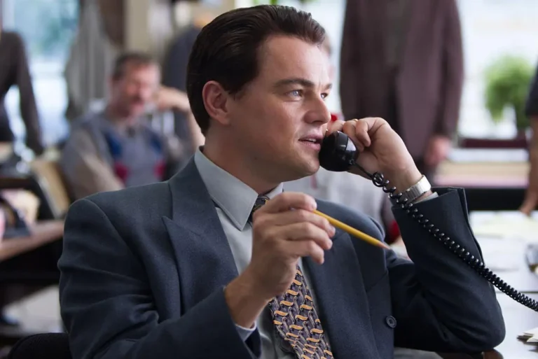 Scène du film le Loupe de Wall Street. Le personnage joué par Leonardo Di Caprio est assis sur une chaise avec un crayon dans la main droite et un téléphone dans la main gauche. Il réalise une vente par téléphone.